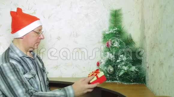 一个戴圣诞老人帽子的人正把圣诞礼物放在圣诞树下视频的预览图