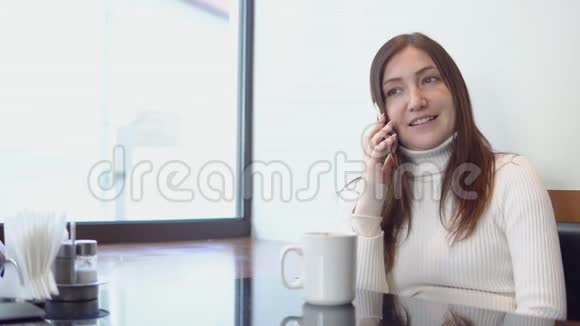 年轻漂亮的女人坐在咖啡馆的桌子旁在打电话视频的预览图