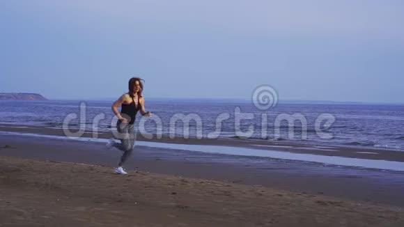 一个夏天的早晨穿着运动制服头发红的苗条中年妇女沿着沙质海岸奔跑视频的预览图