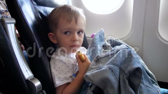 小男孩坐在飞机座位上在飞行中吃东西的4K镜头视频的预览图
