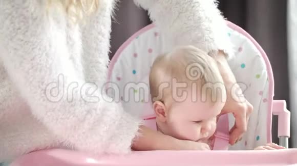 妈妈把婴儿放在厨房的椅子上妈妈的手系好粉色椅子的腰带视频的预览图