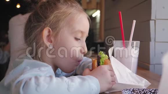 美丽快乐饥饿的女婴在咖啡馆里吃美味的不健康汉堡快餐概念慢动作录像视频的预览图