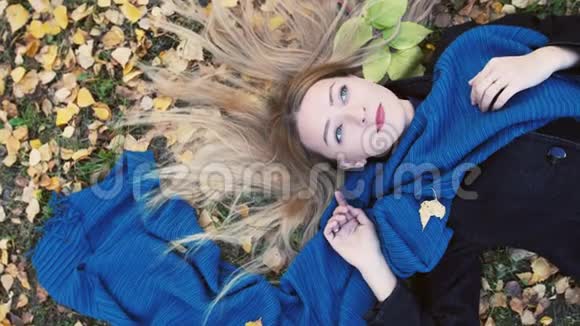 俯瞰秋天金发美女躺在树叶上慢动作3840x2160视频的预览图