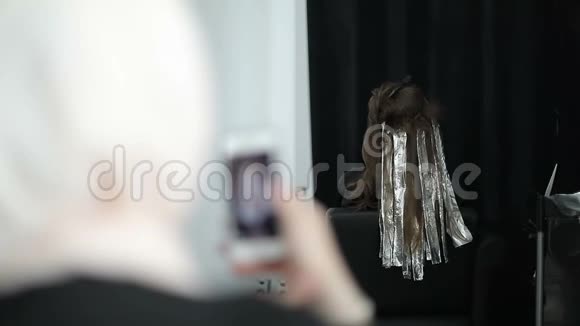 一位戴着围巾的穆斯林妇女在大师班的手机上为染发和理发师拍摄视频视频的预览图