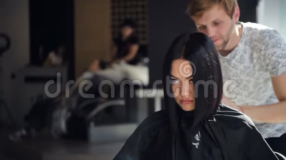 年轻的专业臀部男理发师在沙龙剪客户妇女的黑发视频的预览图