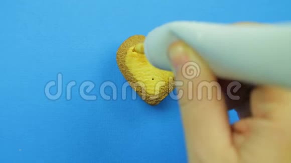 女性的手在蓝色背景上画心形饼干用棕色的管子结冰有趣的脸手工制作视频的预览图