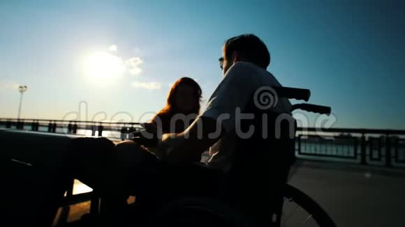 坐在轮椅上和一个女孩在户外聊天的年轻人视频的预览图