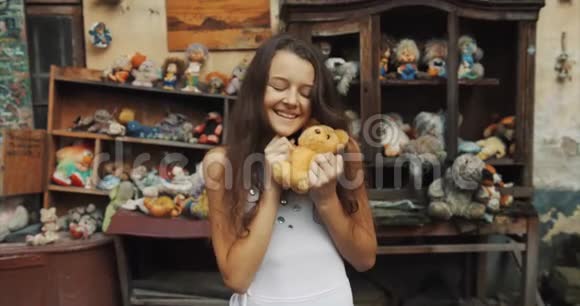 这幅美丽的10岁女孩拿着泰迪熊的肖像可爱地对着花园里充满旧玩具的相机微笑4k视频的预览图