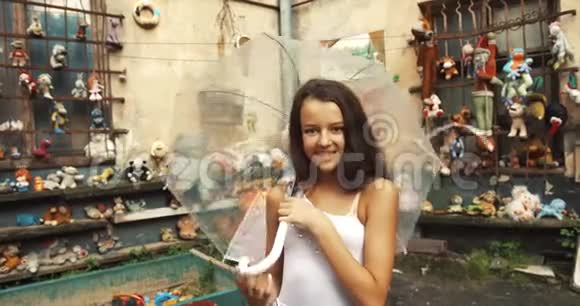 可爱的肖像美丽的女孩与可爱的微笑看着相机旋转一个透明的伞花园视频的预览图