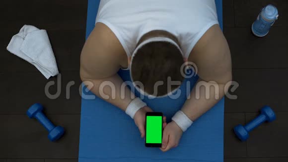 使用在线健身训练应用程序的男性躺在智能手机垫子上视频的预览图