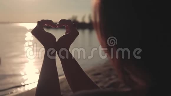 这个女孩在日落时用手做了一个美丽的心的象征视频的预览图