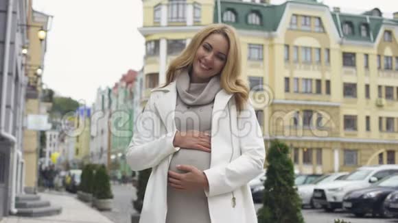 期待幸福的女人看着相机微笑抚摸着腹部母性视频的预览图