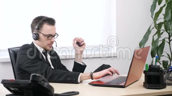 一个穿西装戴眼镜的年轻人为一台笔记本电脑工作并挤压手提扩张器60英尺视频的预览图