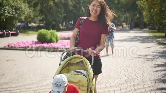 快乐妈妈和小孩子散步一位长相东方的美女带着孩子在城市公园散步慢慢视频的预览图