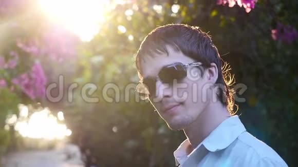 夕阳下戴太阳镜的年轻人在花丛中向太阳招手慢动作1920x1080视频的预览图