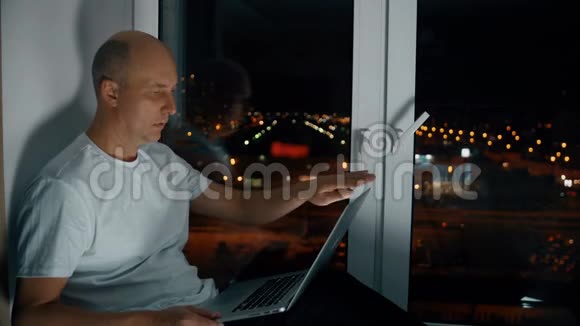 使用笔记本的人坐在窗台上可以看到夜景视频的预览图