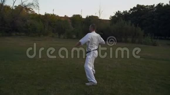 空手道练习者一个穿着白色和服的人一大早就在城市公园的空地上制作卡塔组合视频的预览图