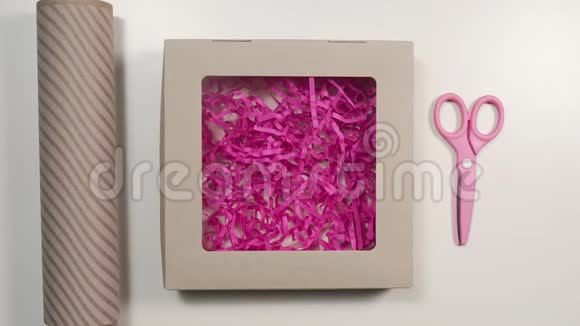 打开带粉色纸的节日盒包装礼物桌上放有剪刀的包装纸DIY包装视频的预览图