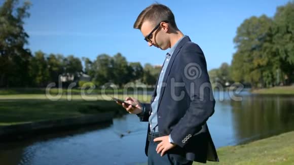 年轻的商人穿着西装戴着太阳镜在一片美丽的风景面前用手机智能手机说话视频的预览图