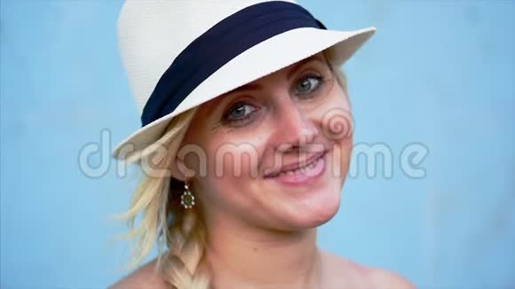 一位美丽的白种人女子的肖像戴着蓝色丝带的白帽子的金发在户外微笑着看着视频的预览图