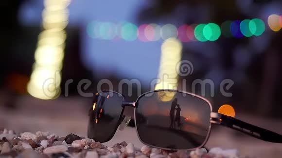 太阳镜躺在热带海滩上年轻的旋转的轮廓在背景上反射慢动作视频的预览图