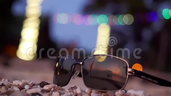 太阳镜躺在热带海滩上年轻的拥抱夫妇的剪影在背景上反射慢动作夏季视频的预览图
