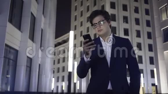 一位严肃的年轻商人带着智能手机和耳机在一个夜城散步视频的预览图