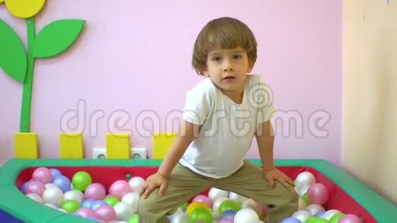 快乐可爱的小男孩蹒跚学步微笑着在多种颜色的球池里玩耍学前教育视频的预览图