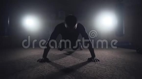 拳击手在黑暗烟雾弥漫的健身房做俯卧撑深色背景下的运动员剪影视频的预览图
