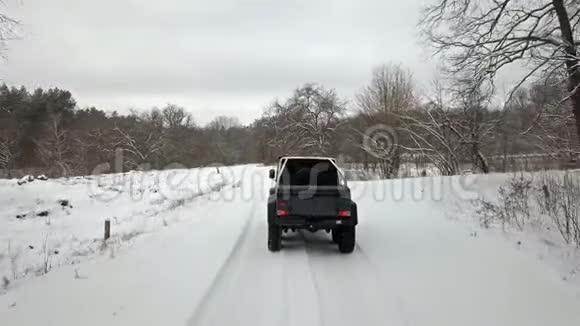 越野车6x6行驶在森林边缘白雪覆盖的乡村道路上后景视频的预览图