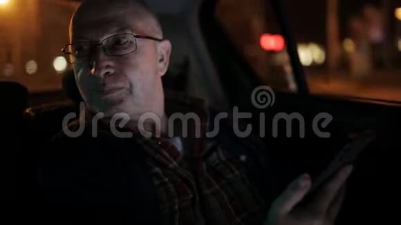 一个在出租车里用手机的老人他在网上发短信查看邮件聊天或新闻晚安视频的预览图