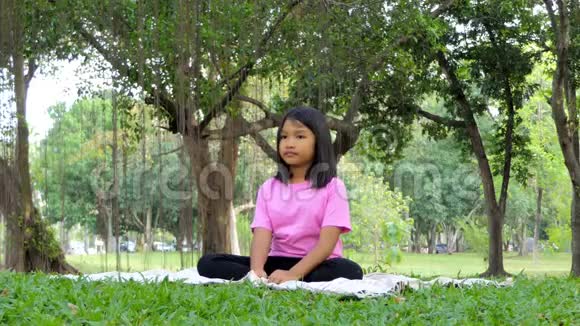 亚洲女孩在公共公园的树下冥想视频的预览图