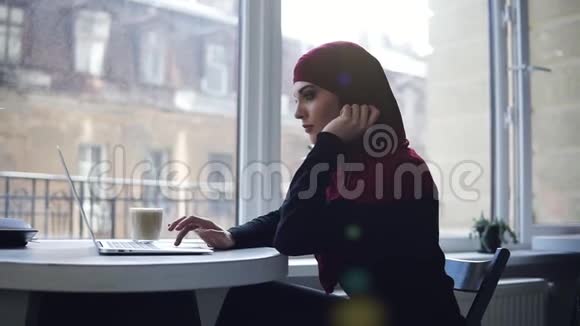 漂亮的穆斯林女孩头上戴着头巾看着她的笔记本电脑屏幕上的东西微笑着印度支视频的预览图