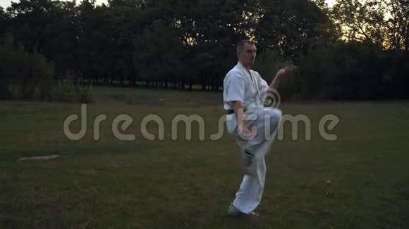 清晨一个穿着白色和服的男人在城市公园里用空手道踢腿视频的预览图