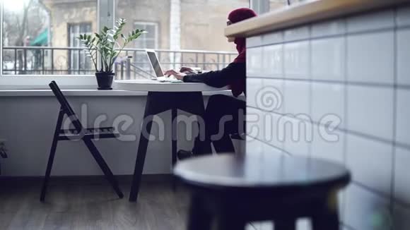 美丽的穆斯林女孩头上戴着头巾坐在窗户附近正在她的键盘上打字视频的预览图