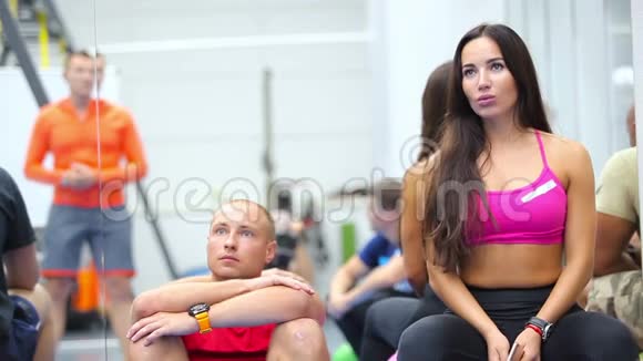 漂亮的女人和年轻人在健身房里听教练训练视频的预览图