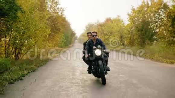秋天一对夫妇骑摩托车在森林道路上的广泛跟踪镜头戴墨镜的漂亮小伙子开车视频的预览图