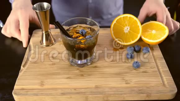 酒精鸡尾酒放在岩石玻璃上木板上有橙色冰和蓝莓双手特写视频的预览图