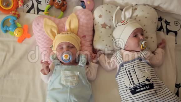 婴儿双胞胎戴着可爱帽子的孩子在竞技场睡觉吸吮奶嘴奶嘴视频的预览图