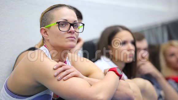 戴眼镜的年轻女子在健身房里听教练训练视频的预览图