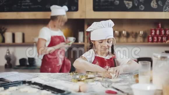 小可爱的女孩在舒适的厨房做饭在做蛋糕和饼干的时候玩得开心她妈妈在后台视频的预览图