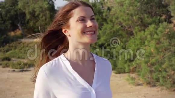 描绘了年轻女子在绿色公园散步的幸福微笑风慢慢地吹着她的头发视频的预览图