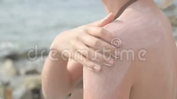 一个迷人的年轻女孩在阳光明媚的夏天坐在海滨在她的肩膀上涂上防晒霜夏季视频的预览图