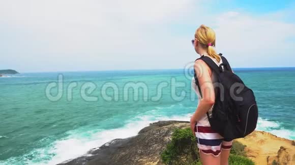 女孩站在岩石的边缘看着海浪热带岛屿之旅视频的预览图