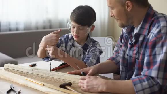父亲教他微笑的儿子木工小男孩在车间用螺丝工视频的预览图