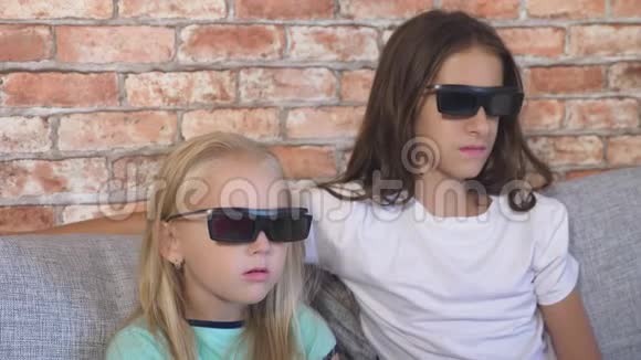差不多了两个戴着3D眼镜的小女孩坐在客厅的沙发上带着许多情绪看着电影视频的预览图