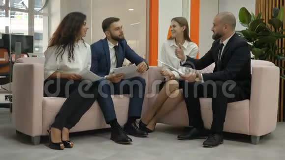 办公室工作人员两名年轻男子和两名年轻妇女男子坐在沙发上讨论公司的重要文件以及视频的预览图
