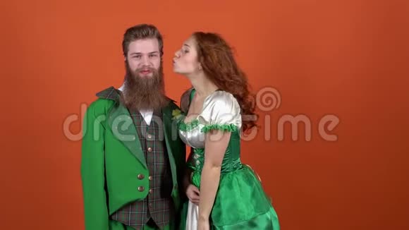 穿着圣诞服装庆祝圣帕特里克节的年轻一对夫妇橙色墙上的女孩接吻视频的预览图