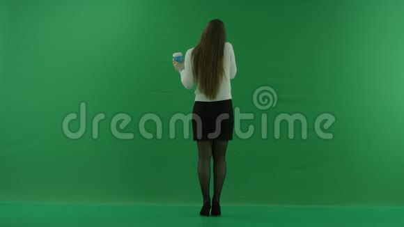 女孩站在镜头前打着电话在绿色的屏幕上喝着一杯视频的预览图