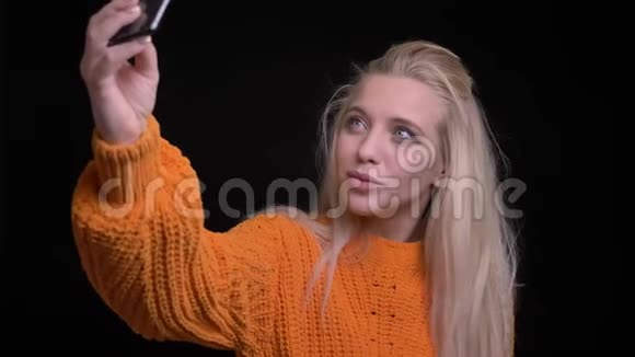特写镜头拍摄年轻漂亮的白种人女性在手机上自拍在镜头前微笑摆姿势视频的预览图